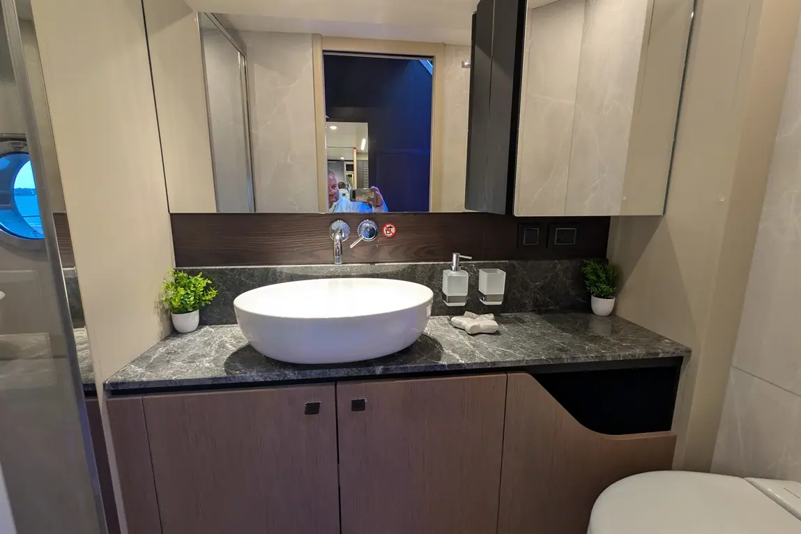 Modern bathroom featuring a white basin, grey countertop, potted plant, and mirrors reflecting the stylish interior design.